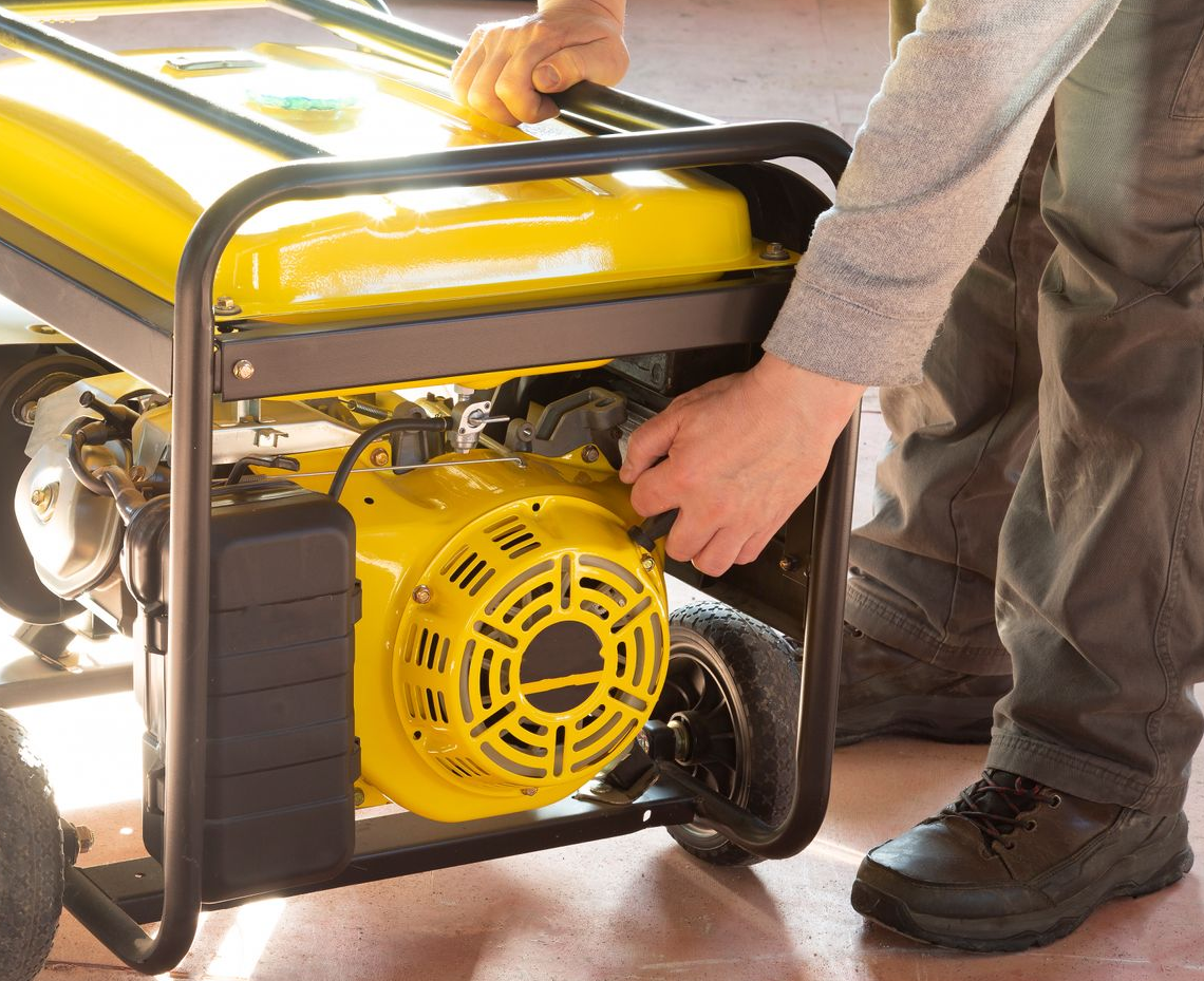A person pulls the recoil starter handle on a portable yellow generator.