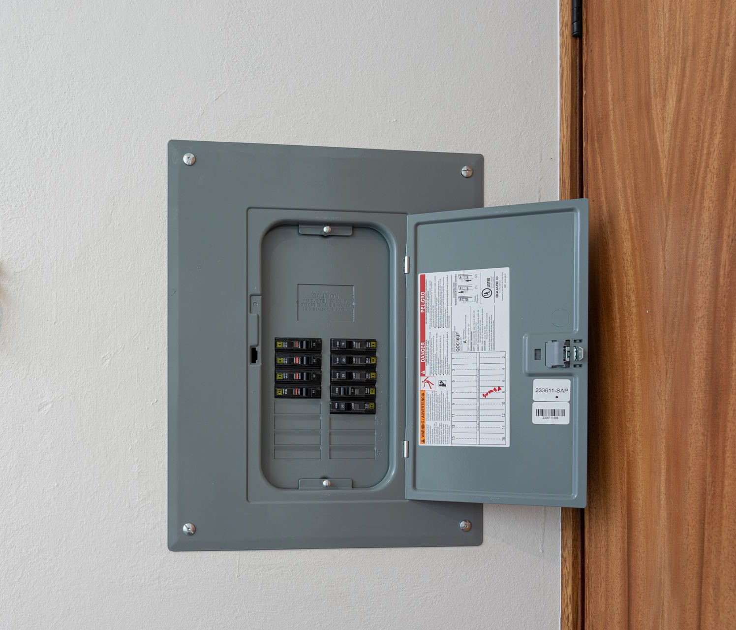 An open grey electrical breaker panel mounted on a white wall next to a wooden door frame.