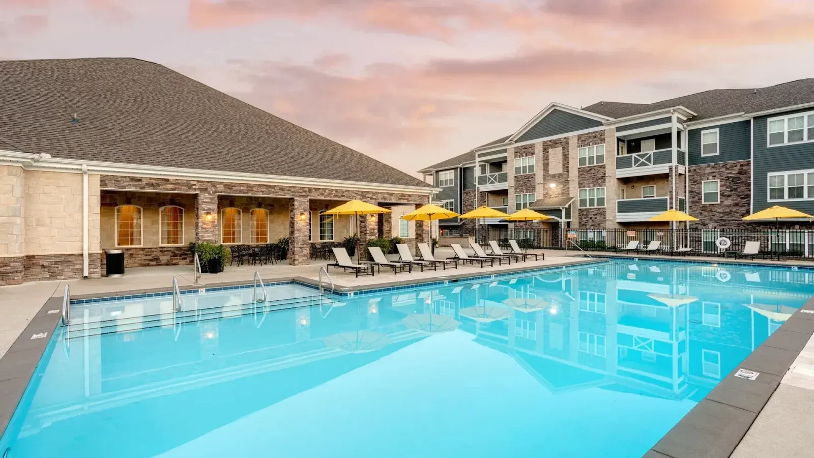 Outdoor resort pool with lounge chairs and a hotel building at sunset