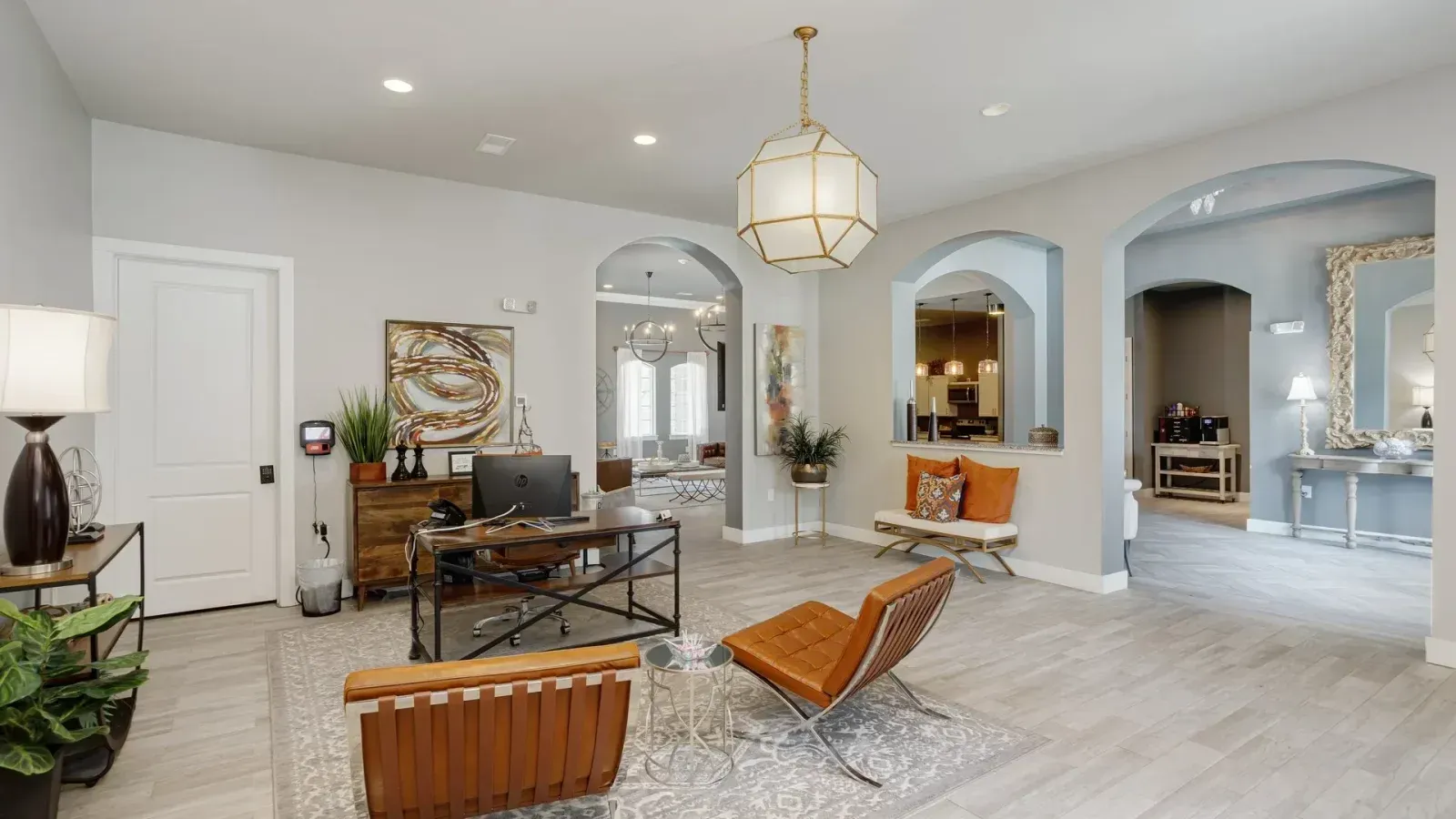 Bright modern living room with arched doorways, white walls, and brown leather chairs around a rug.
