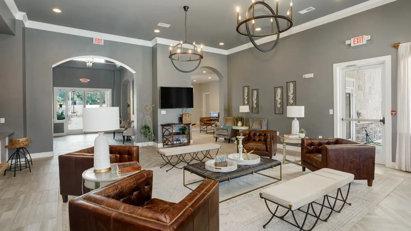 Elegant gray living room with modern seating, chandeliers, fireplace, and TV area