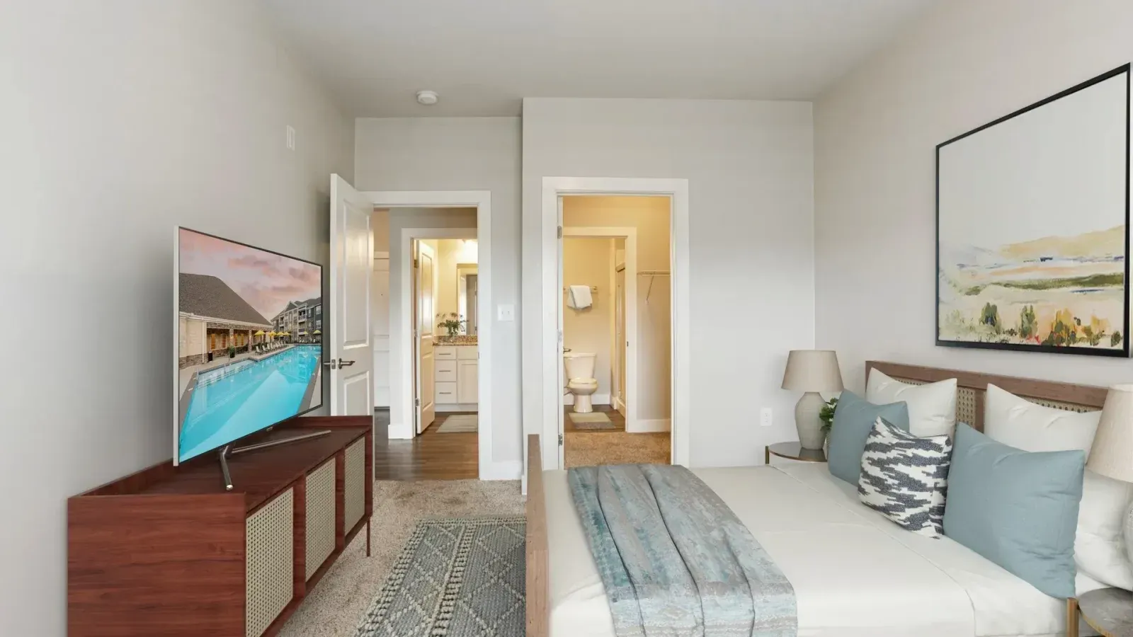 Bright modern bedroom with a bed, TV on a dresser, and an open bathroom visible through the doorway