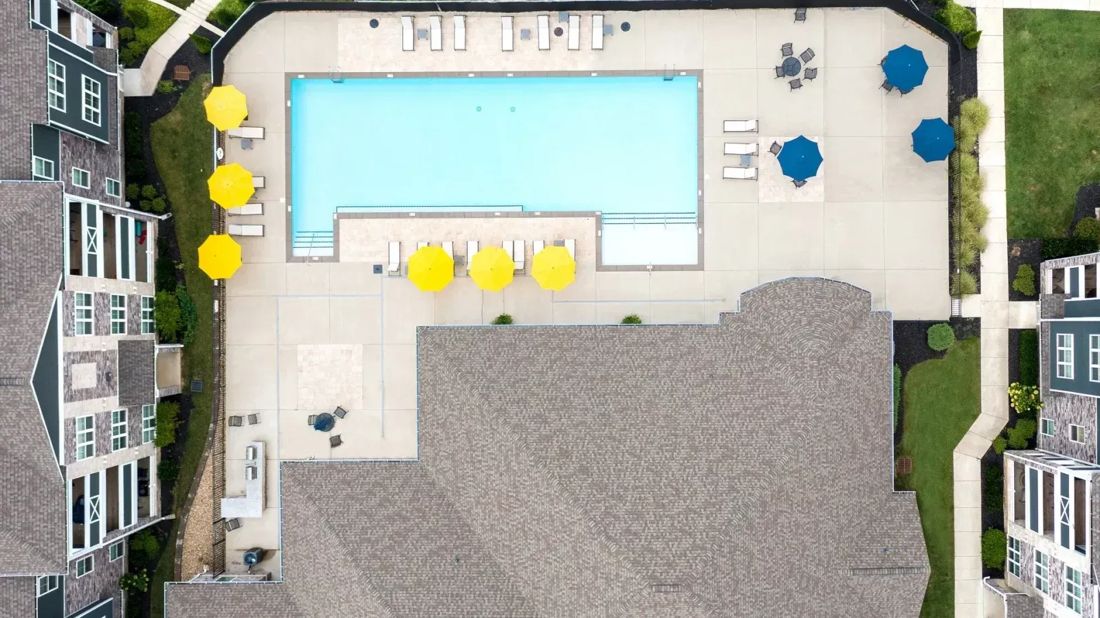 Aerial view of a backyard with a rectangular pool, patio furniture, and surrounding buildings.