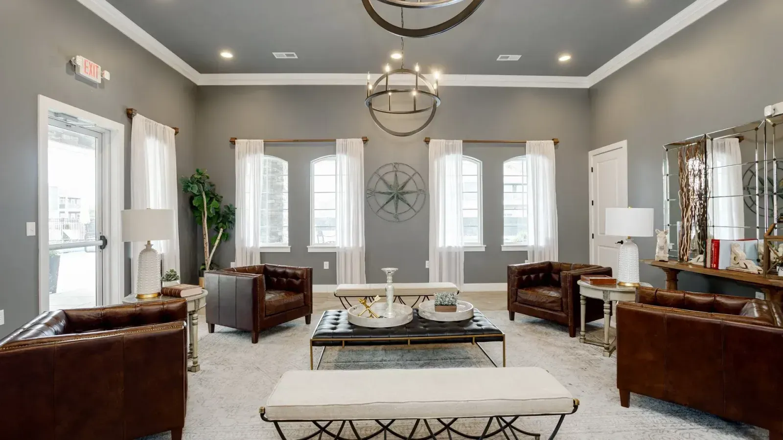 Bright modern living room with gray walls, white shutters, leather chairs, and a glass coffee table