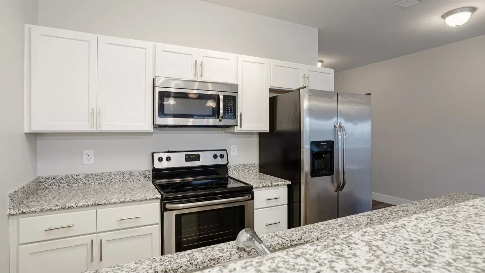 Bright modern kitchen with white cabinets, stainless steel appliances, and speckled granite countertops