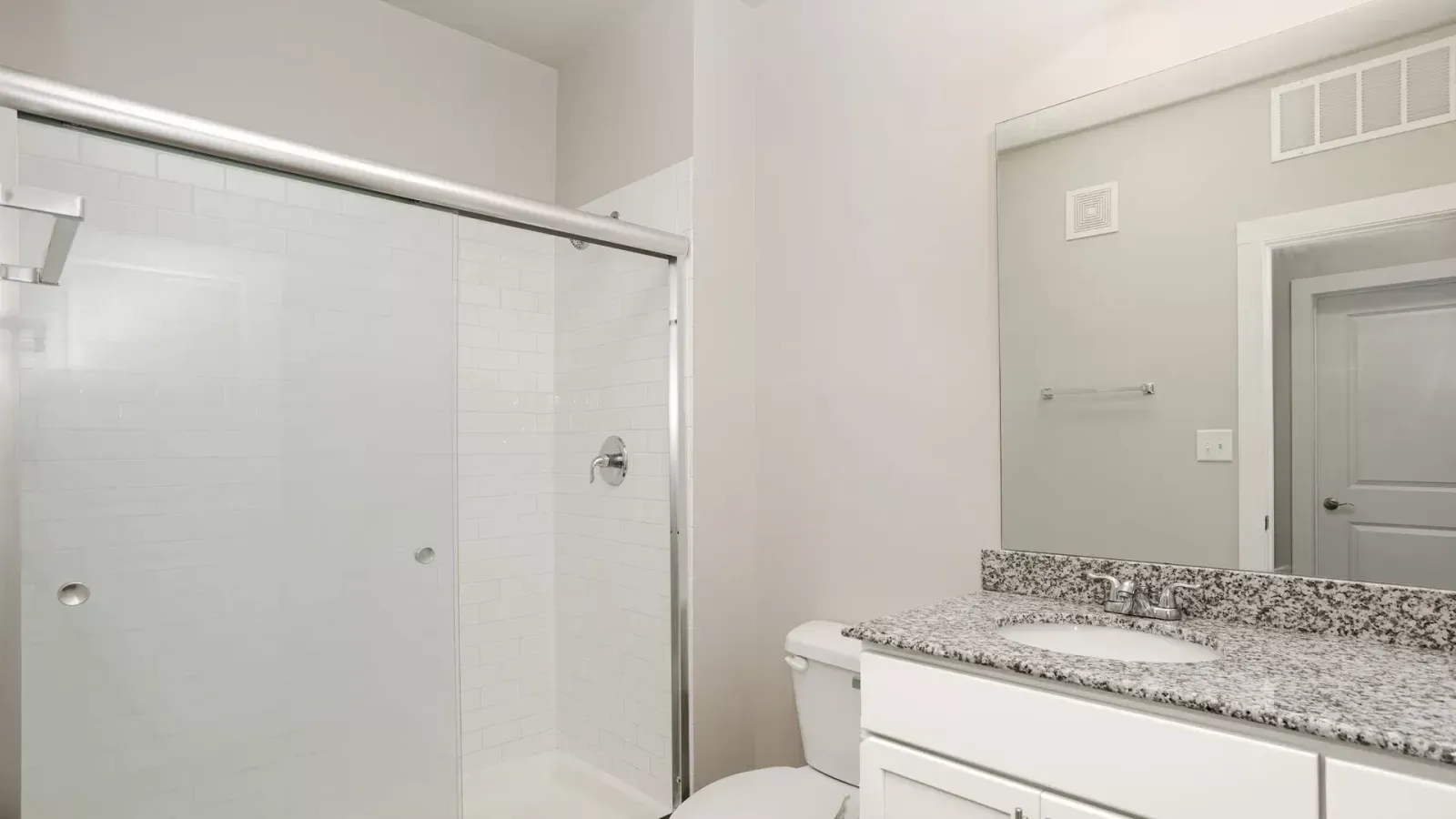 Bright bathroom with a glass shower enclosure, mirror, and granite countertop vanity.