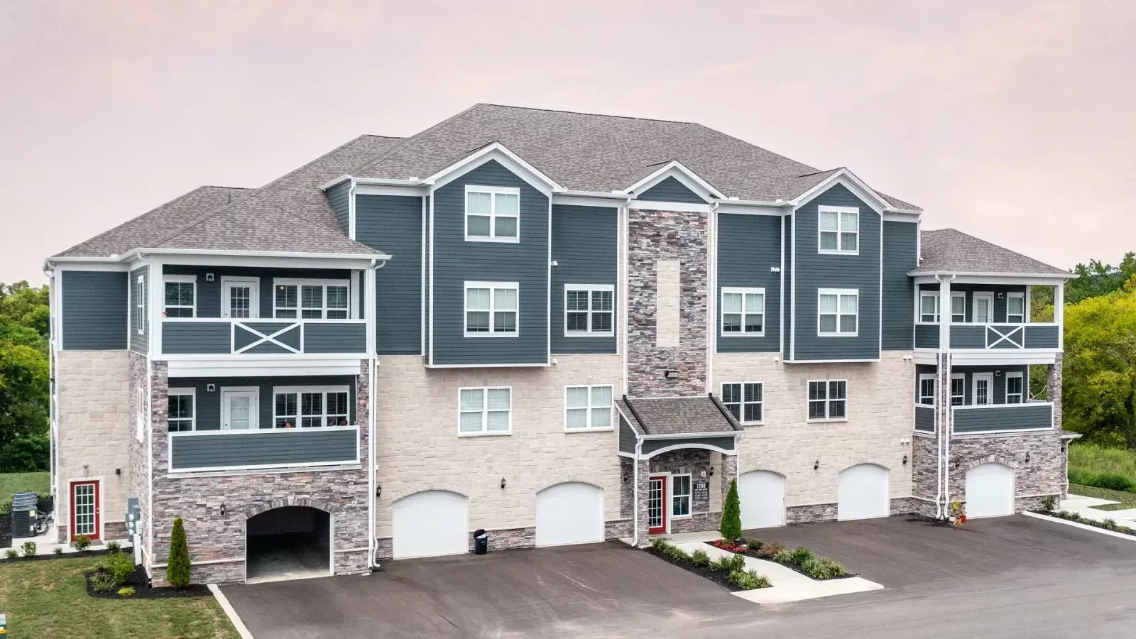 Modern apartment building with gray siding, stone accents, balconies, and a paved parking area