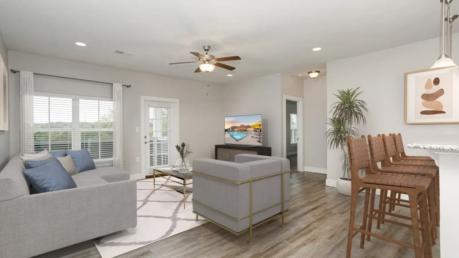 Bright open living room with gray sofa, wood floors, TV, plants, and a wooden dining table and chairs.