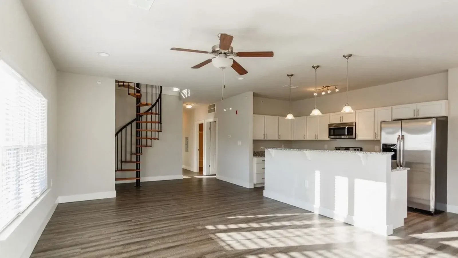 Open-concept kitchen and living room with white cabinets, island, ceiling fan, staircase, and stainless steel appliances