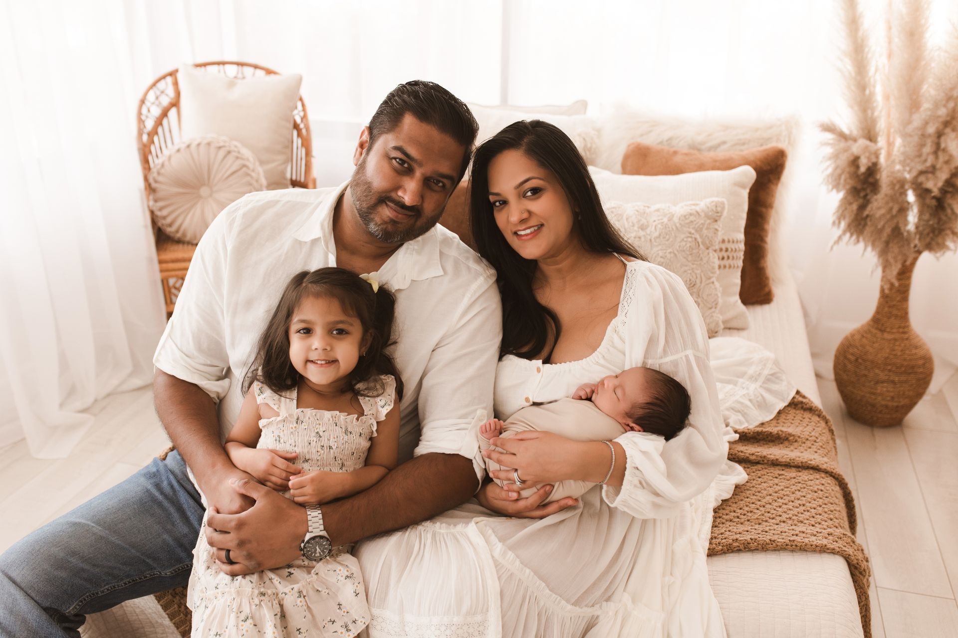 Family of four sitting together on a bed in a bright, cozy bedroom.