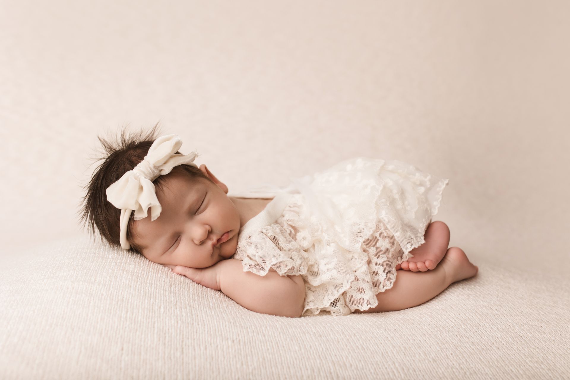 Sleeping baby in a white lace dress and headband on a soft cream blanket