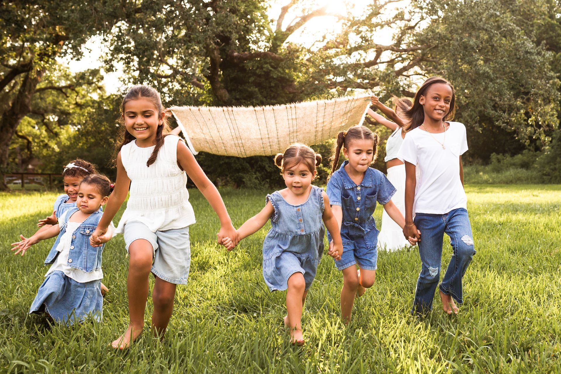 Children running hand-in-hand through a grassy field, smiling in bright daylight.