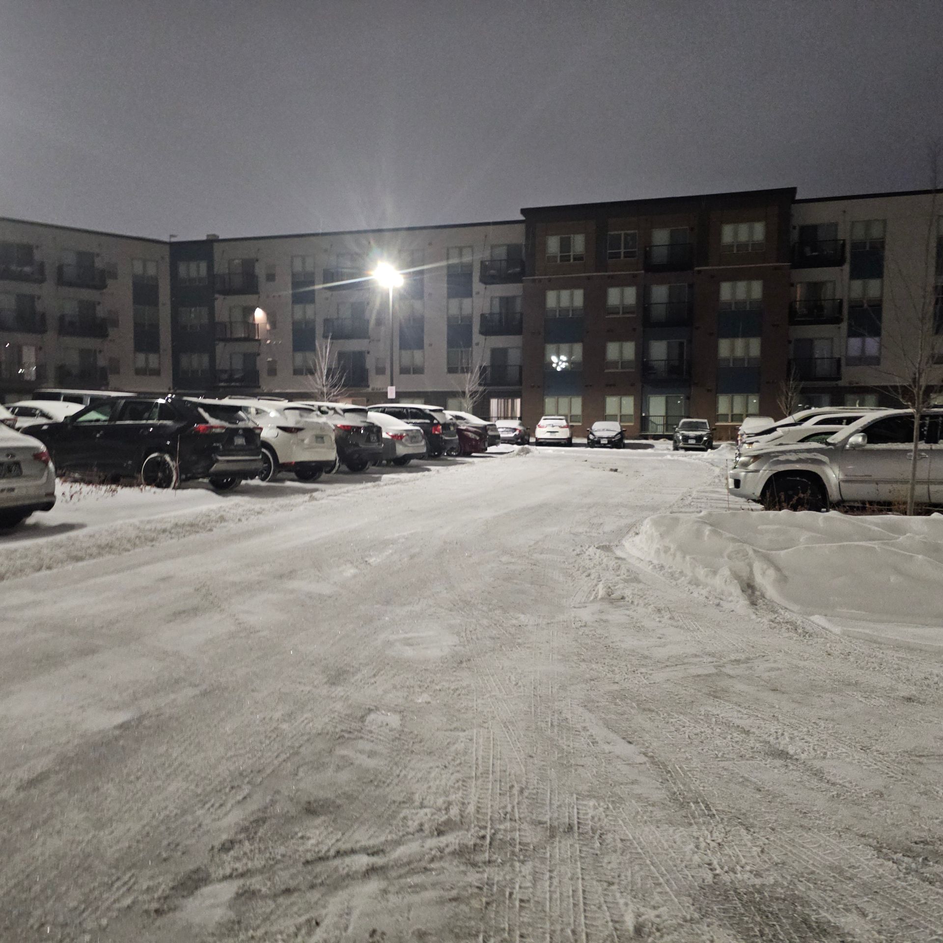 A lot of cars are parked in a snowy parking lot