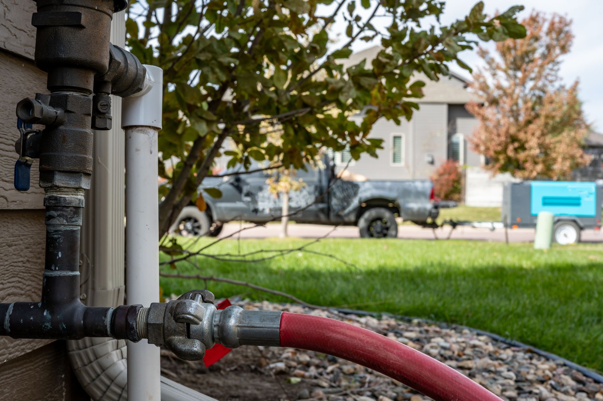 A red hose is attached to a pipe on the side of a house.