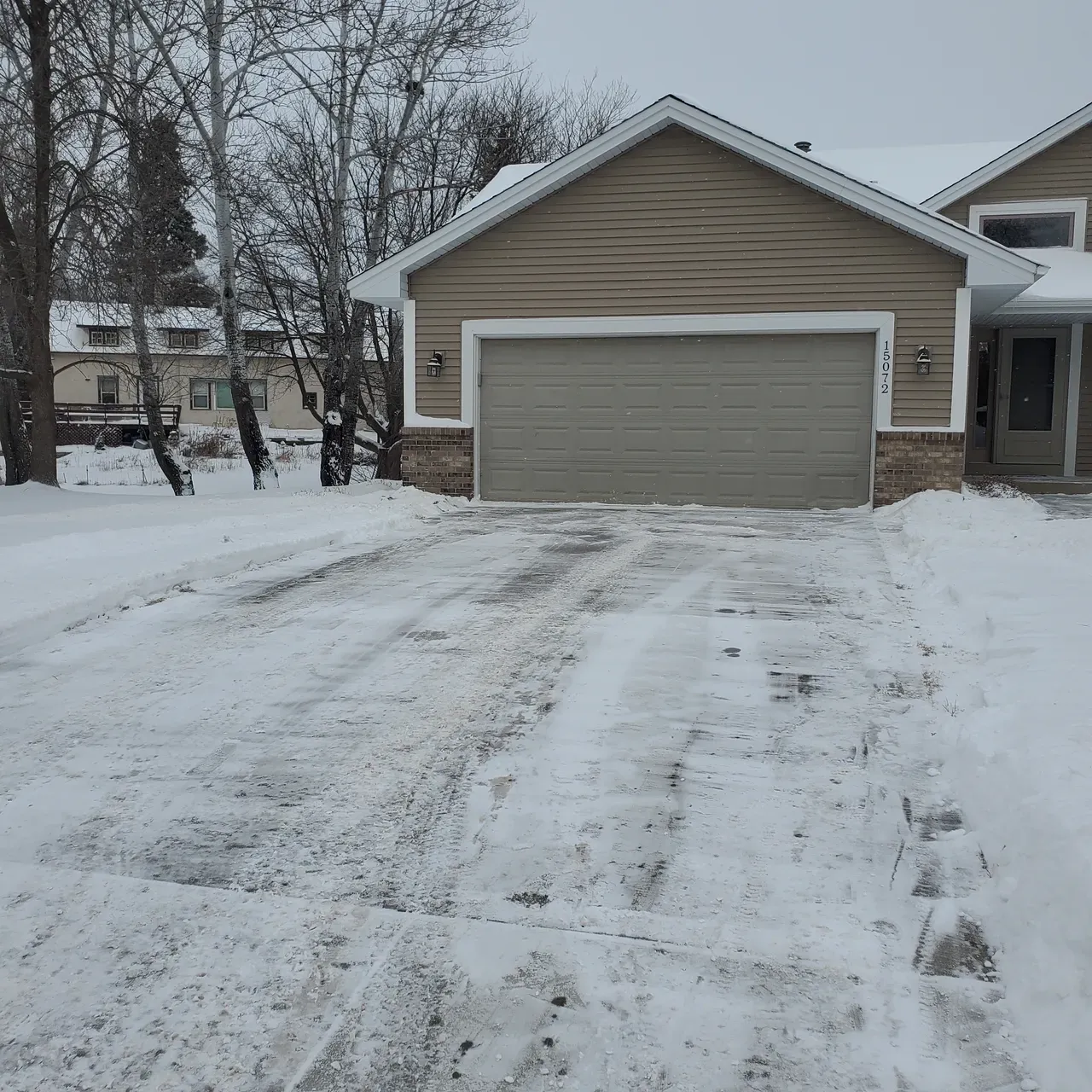 A snowy driveway leading to a house with a garage door