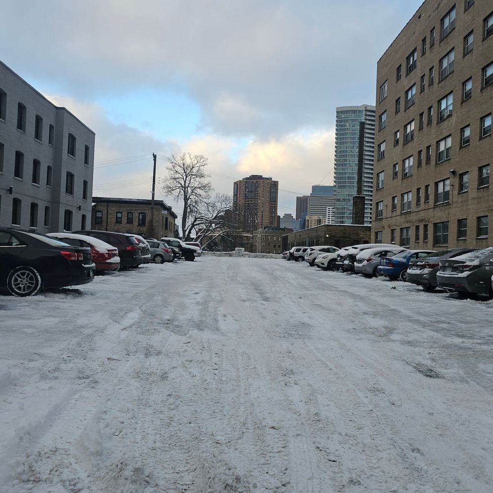 A snowy parking lot with cars parked in front of buildings