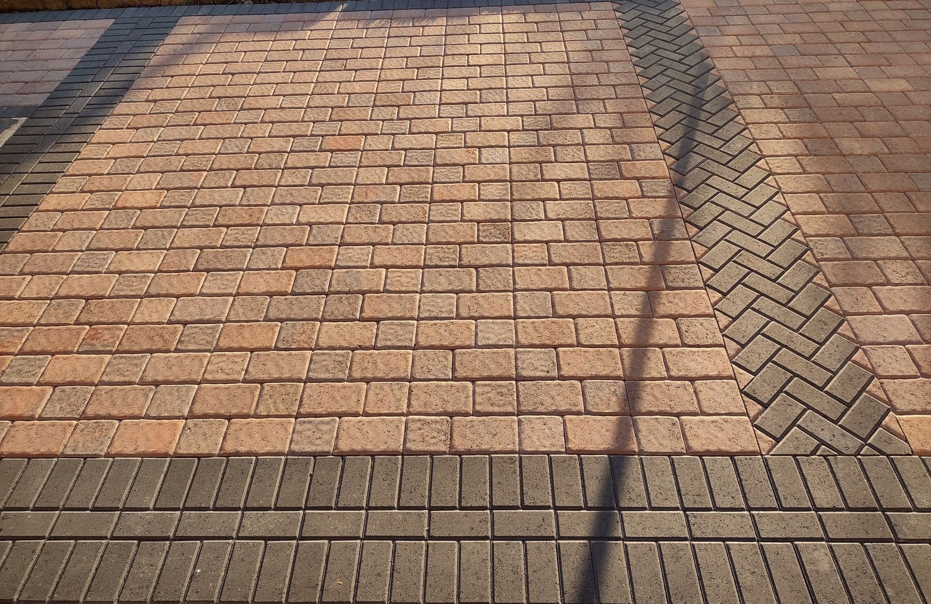 Brick-paved walkway with diagonal shadows and a darker herringbone border path