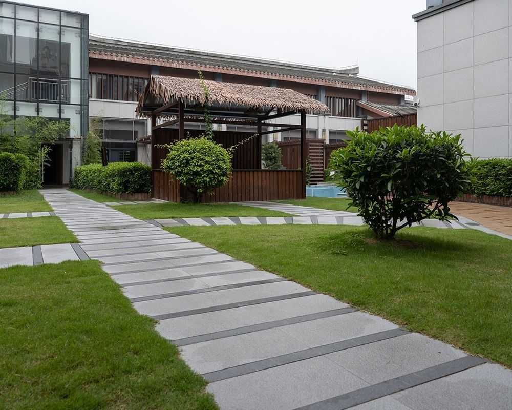 Stone walkway leading to a wooden gazebo in a landscaped courtyard with green grass and shrubs