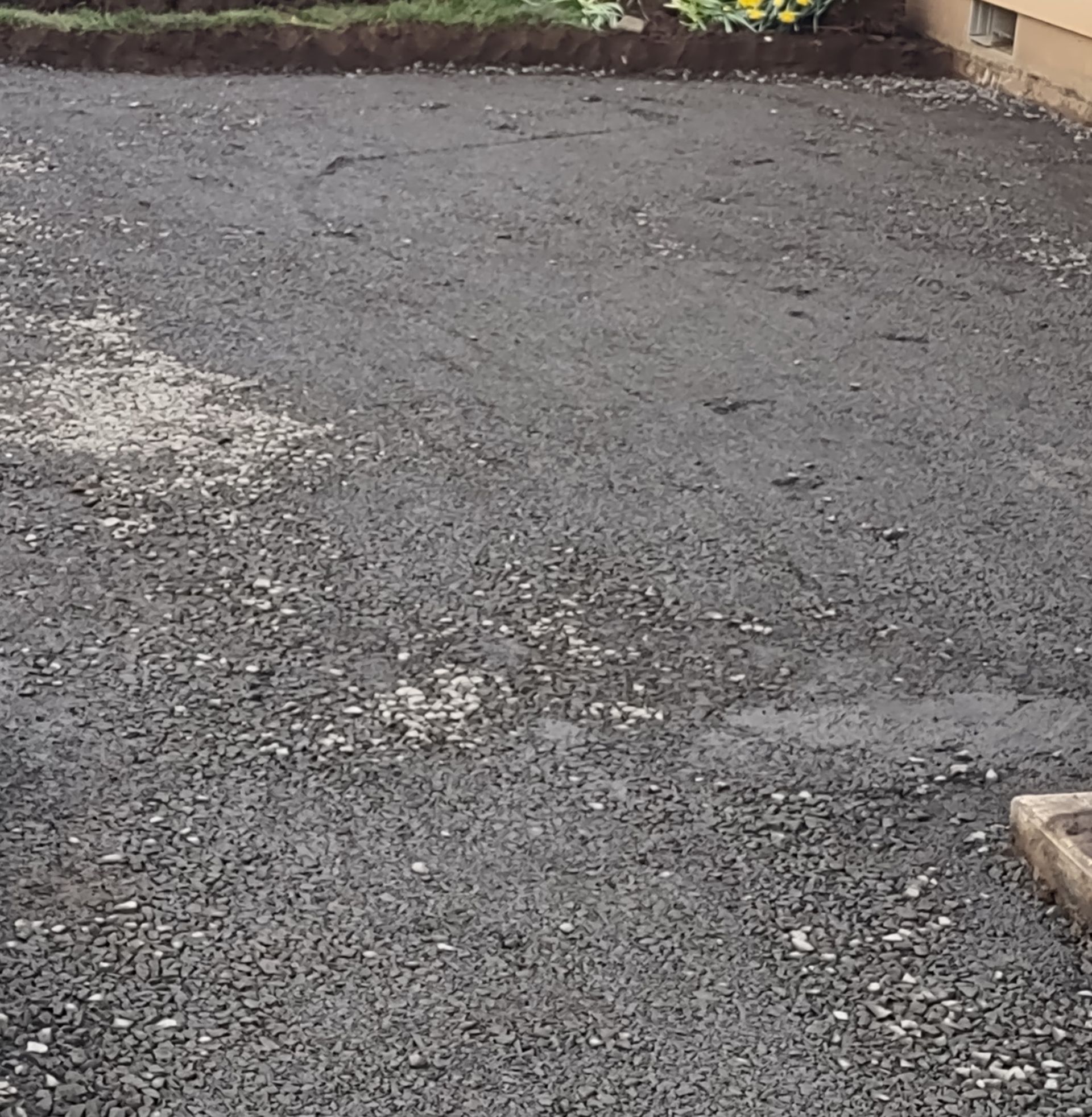 Gravel driveway or yard with patchy gray surface and a building edge on the right