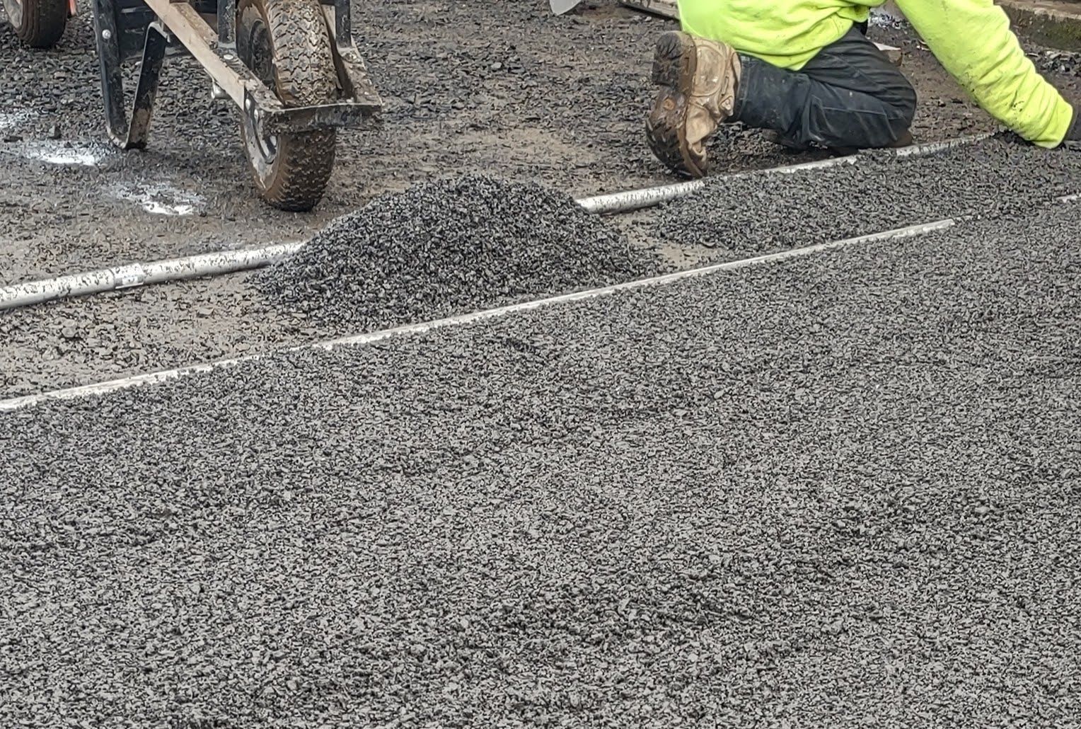 Workers paving a wet road with fresh asphalt and road markings visible