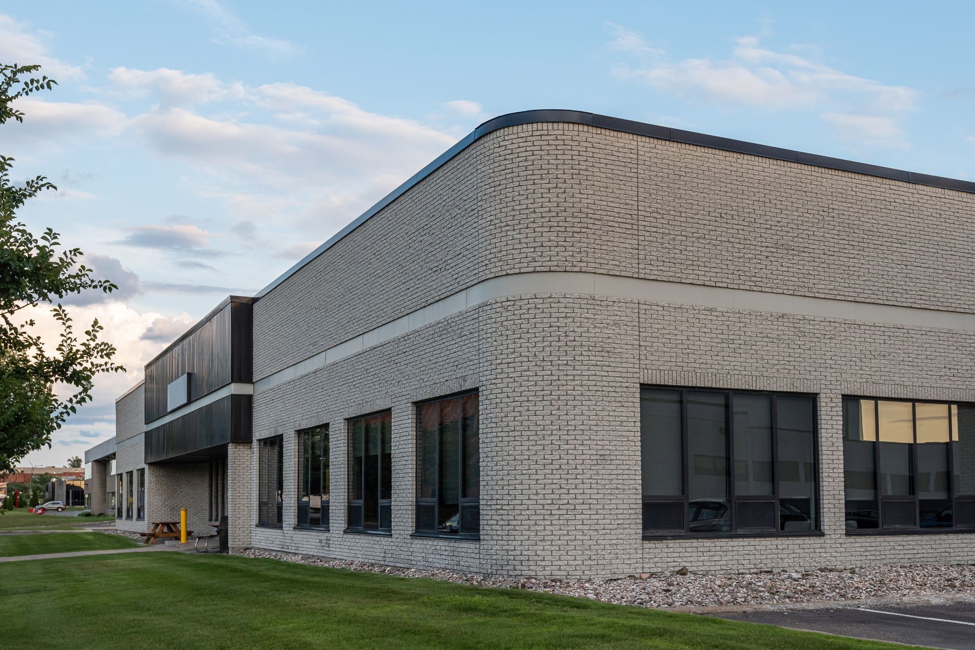 Modern gray industrial building with dark windows and a manicured lawn under a cloudy sky