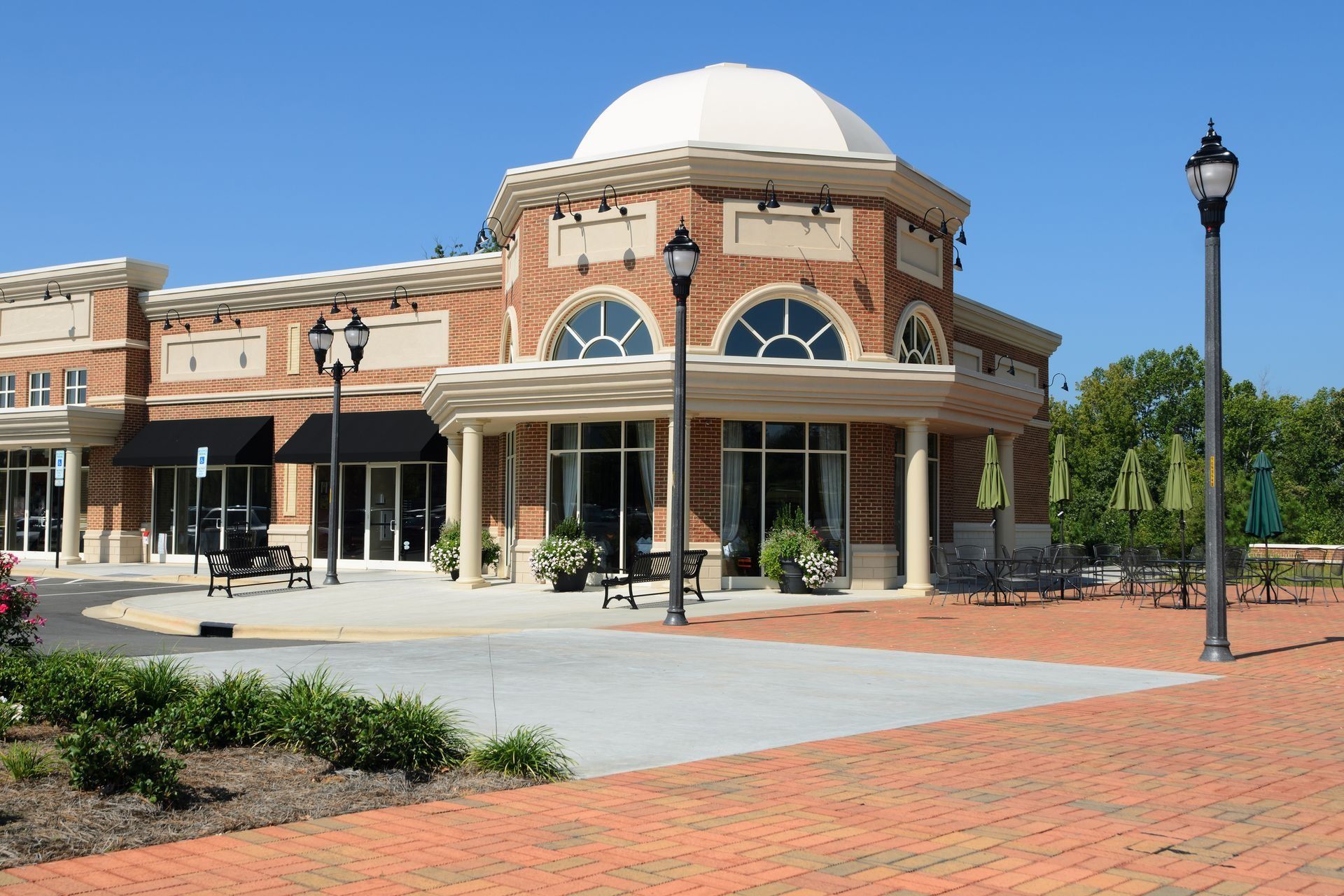 Brick building with a white dome and storefronts on a sunny plaza with brick paving