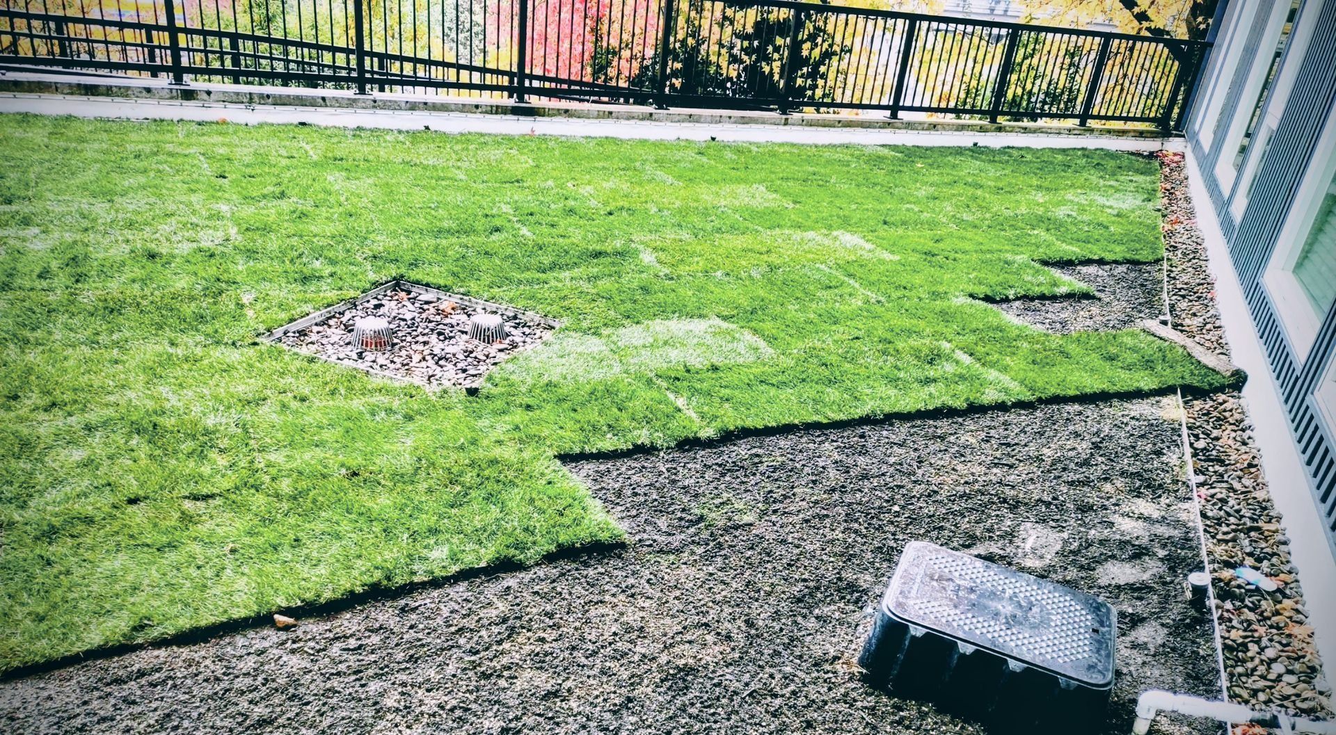 Small fenced yard with green grass, gravel path, and a pile of dirt near the center.