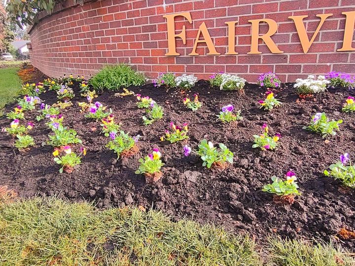 Fairview brick sign behind colorful flowers and mulch bed