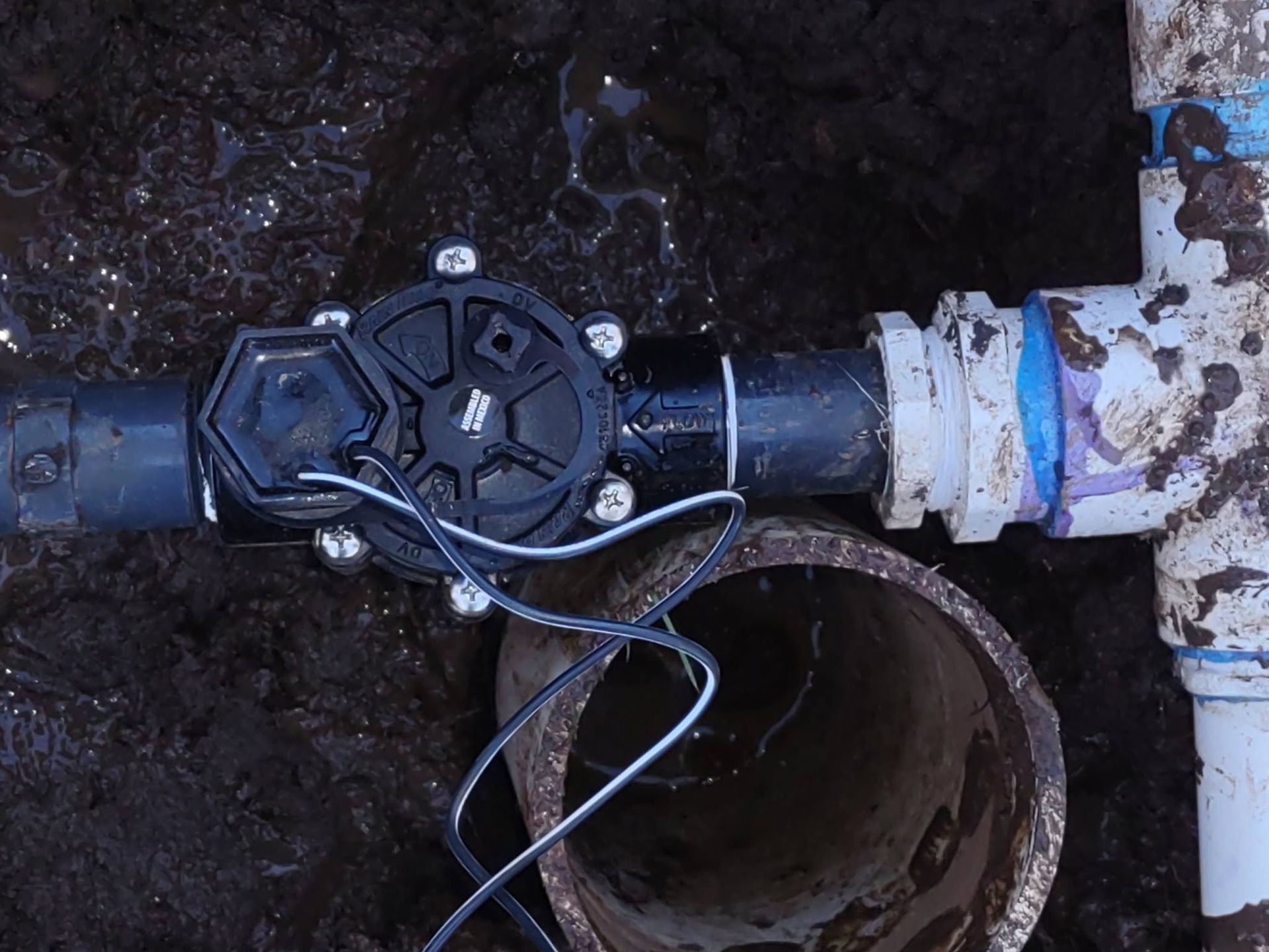 Open water valve on a blue pipe in a muddy underground utility pit