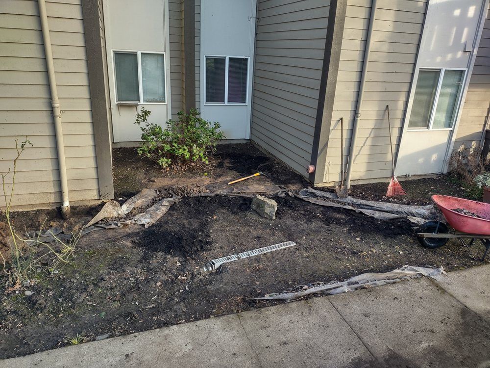 Damaged dirt patch and walkway beside a beige townhouse, with exposed soil and scattered debris.