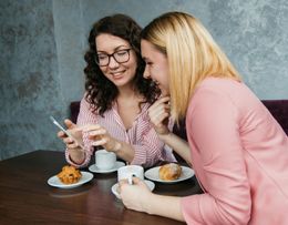Two women are sitting at a table looking at a cell phone.