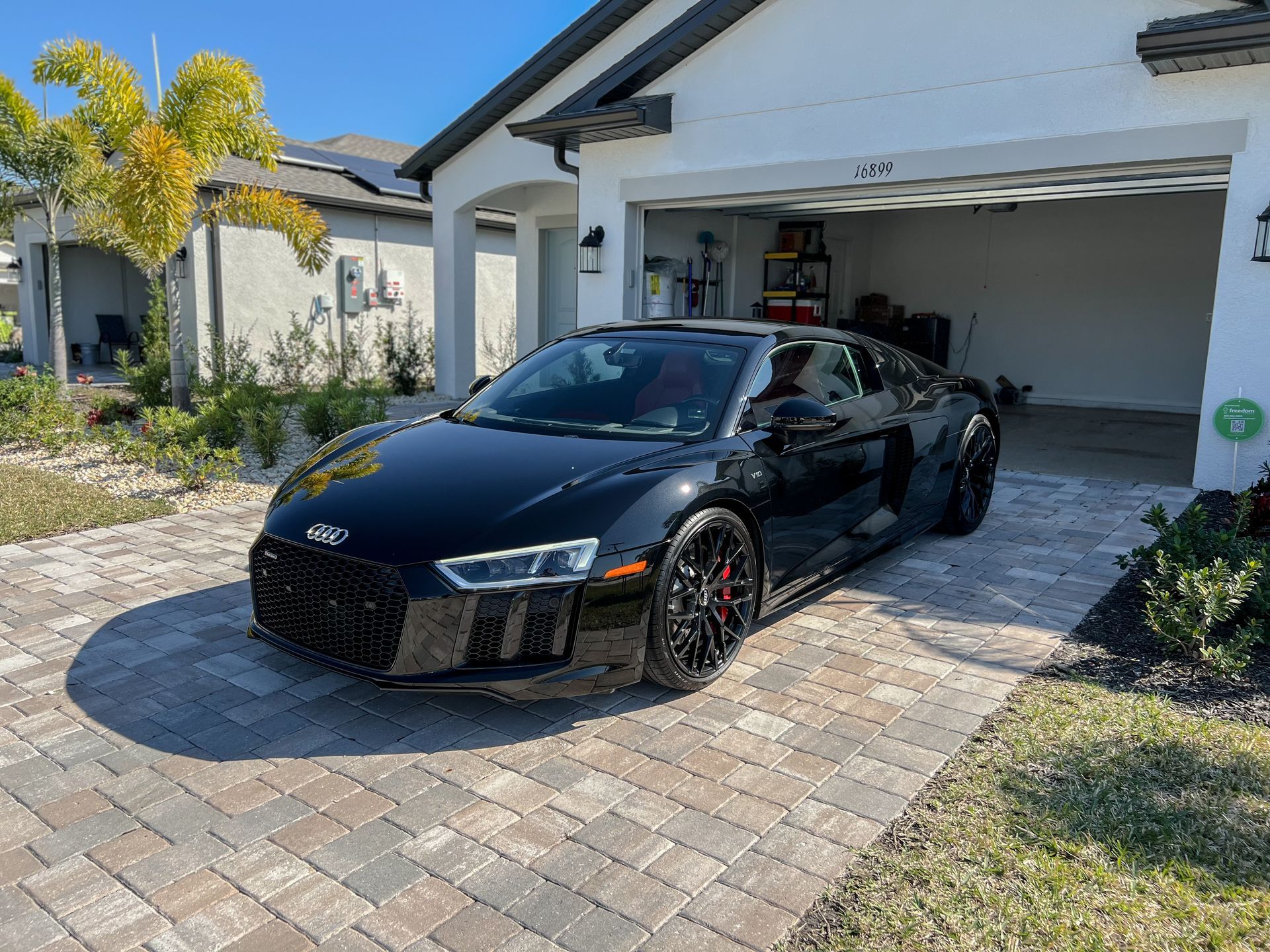Black Audi R8 sports car parked in front of a white house with an open garage.