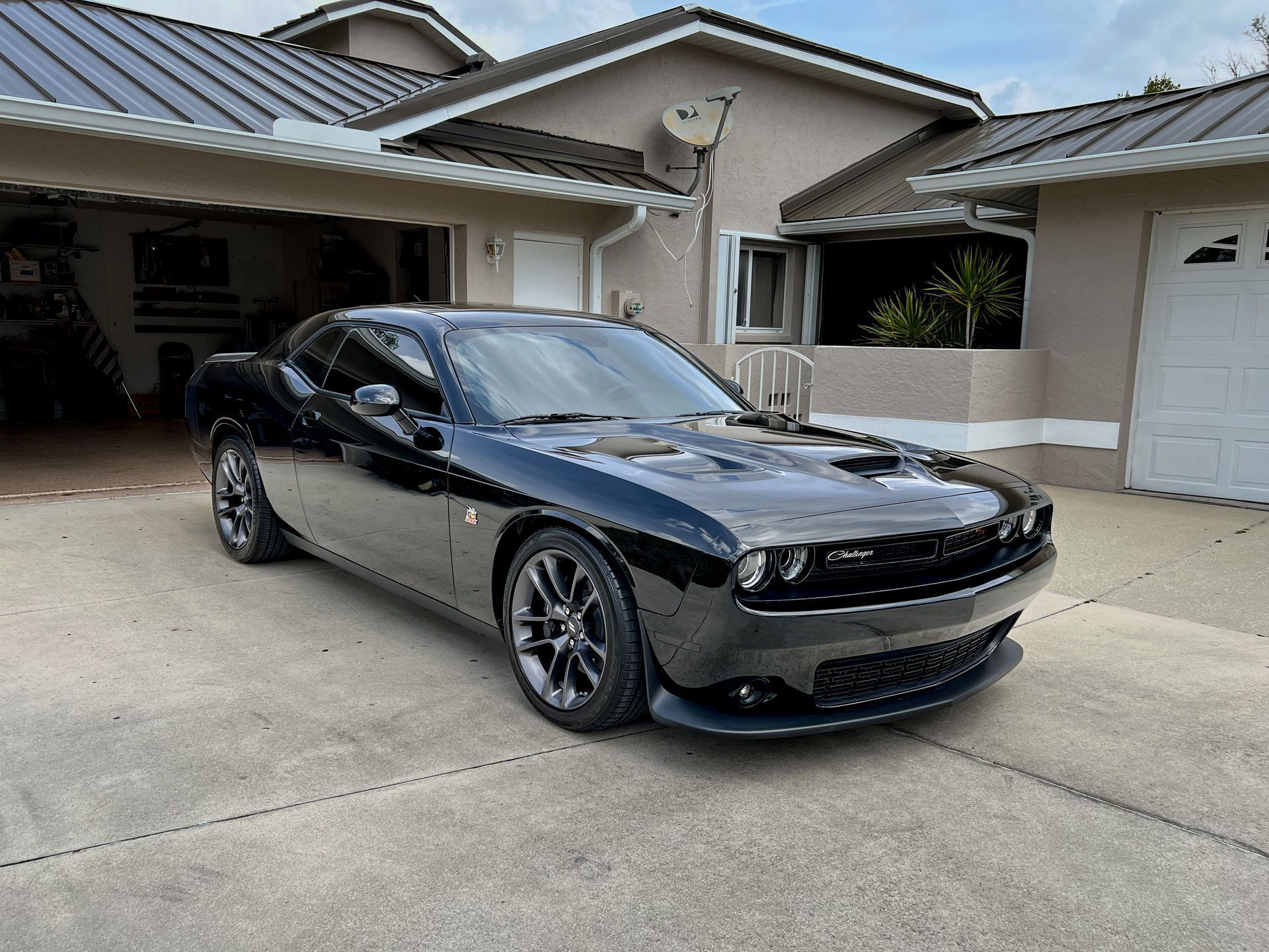 Black Dodge Challenger parked in a driveway in front of a house.