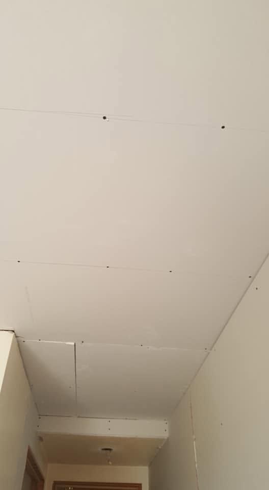 Bare white drywall ceiling in a narrow hallway, with seams and small dark screw points visible.