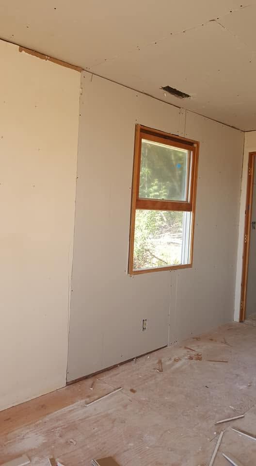 Empty room under renovation with unfinished walls, exposed floor, and a window letting in daylight
