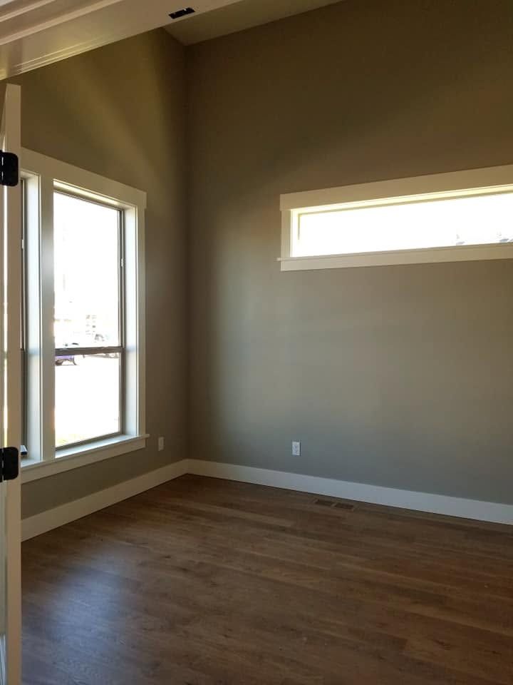 Empty unfurnished room with wood floors, beige walls, and two windows letting in daylight