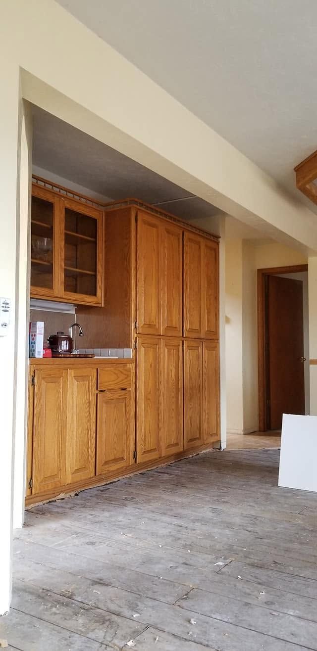 Empty kitchen with wooden cabinets and unfinished floor beneath a doorway opening