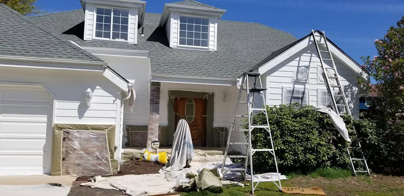 White house exterior with damaged roof, white porch chairs, and ladder in front yard.