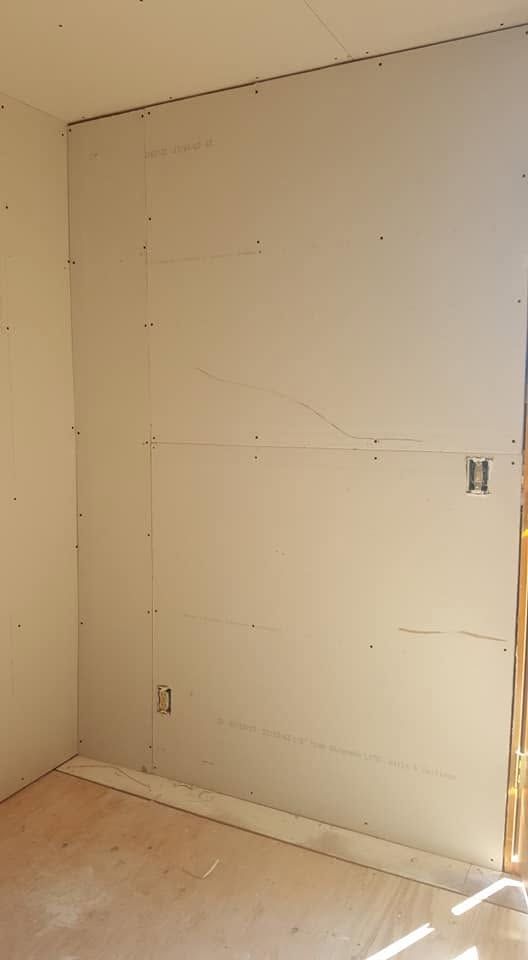 Bare unfinished drywall wall in a room, with visible seams and an electrical box opening.
