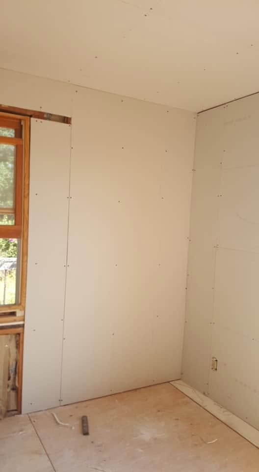 Empty unfinished room with white drywall, a window on the left, and a bare floor under construction