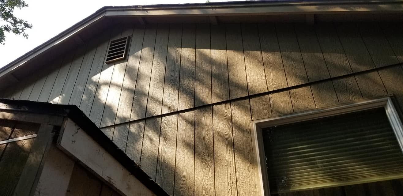 Exterior of a beige house with a slanted roof, vent, and window shutters in sunlight