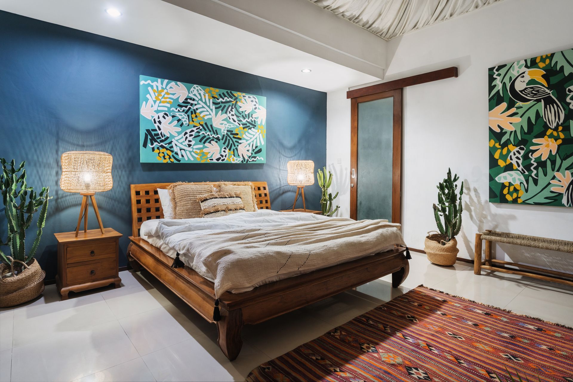 Cozy bedroom with wooden bed, blue accent wall, lamps, and tropical artwork