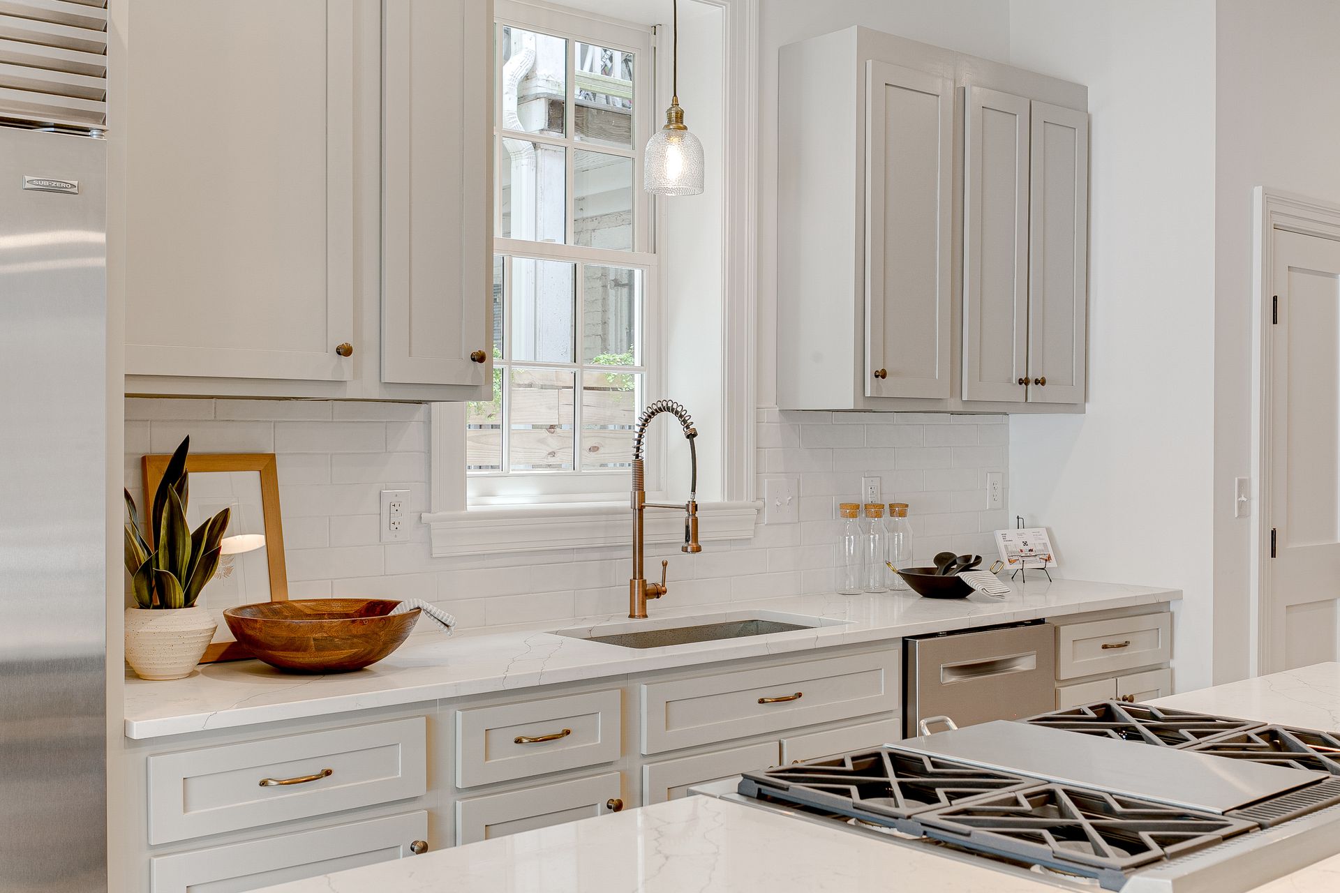 Bright white kitchen with marble counters, window above sink, and gas range in foreground