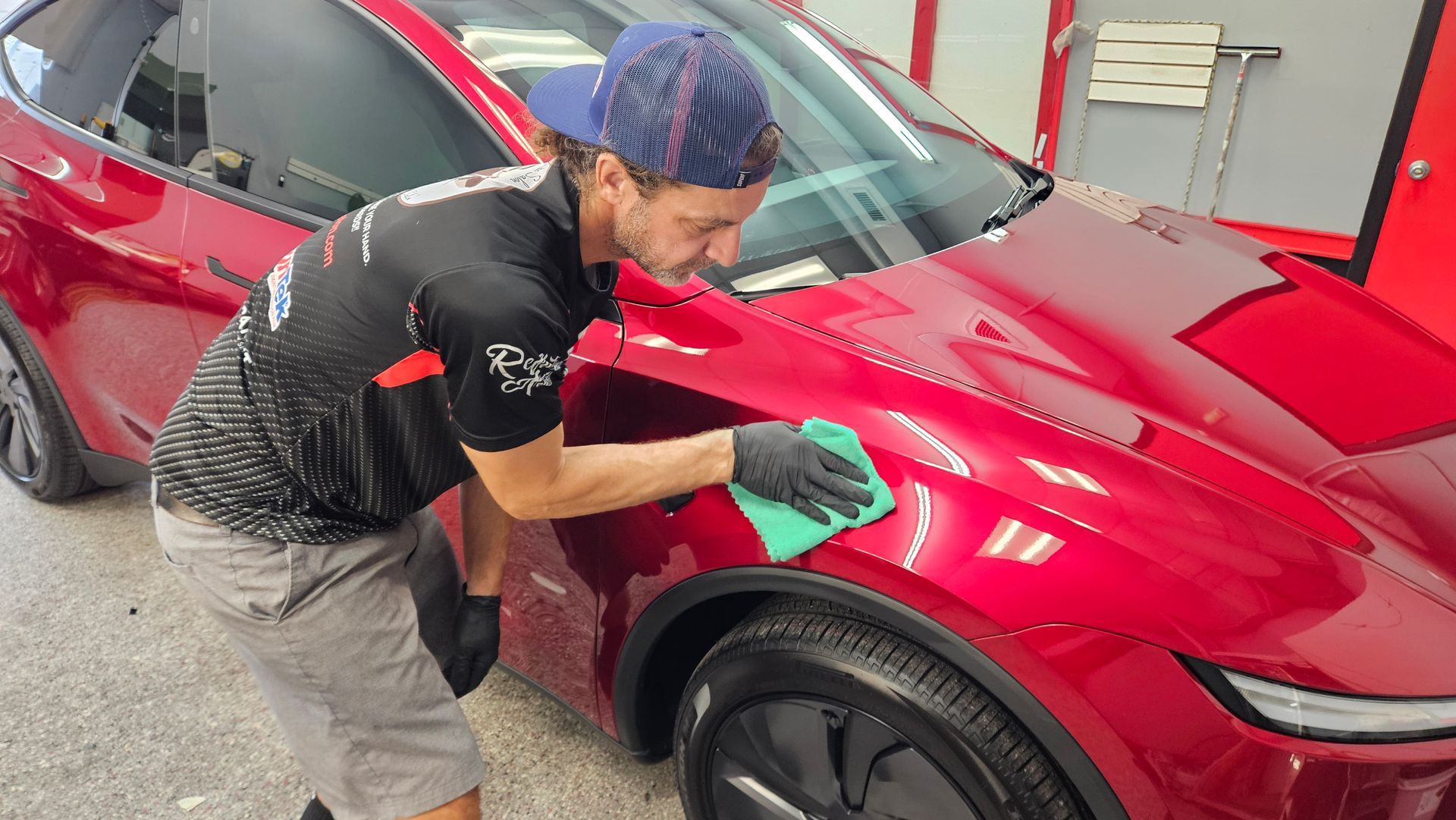 Technician polishing a red car’s front fender in an auto shop