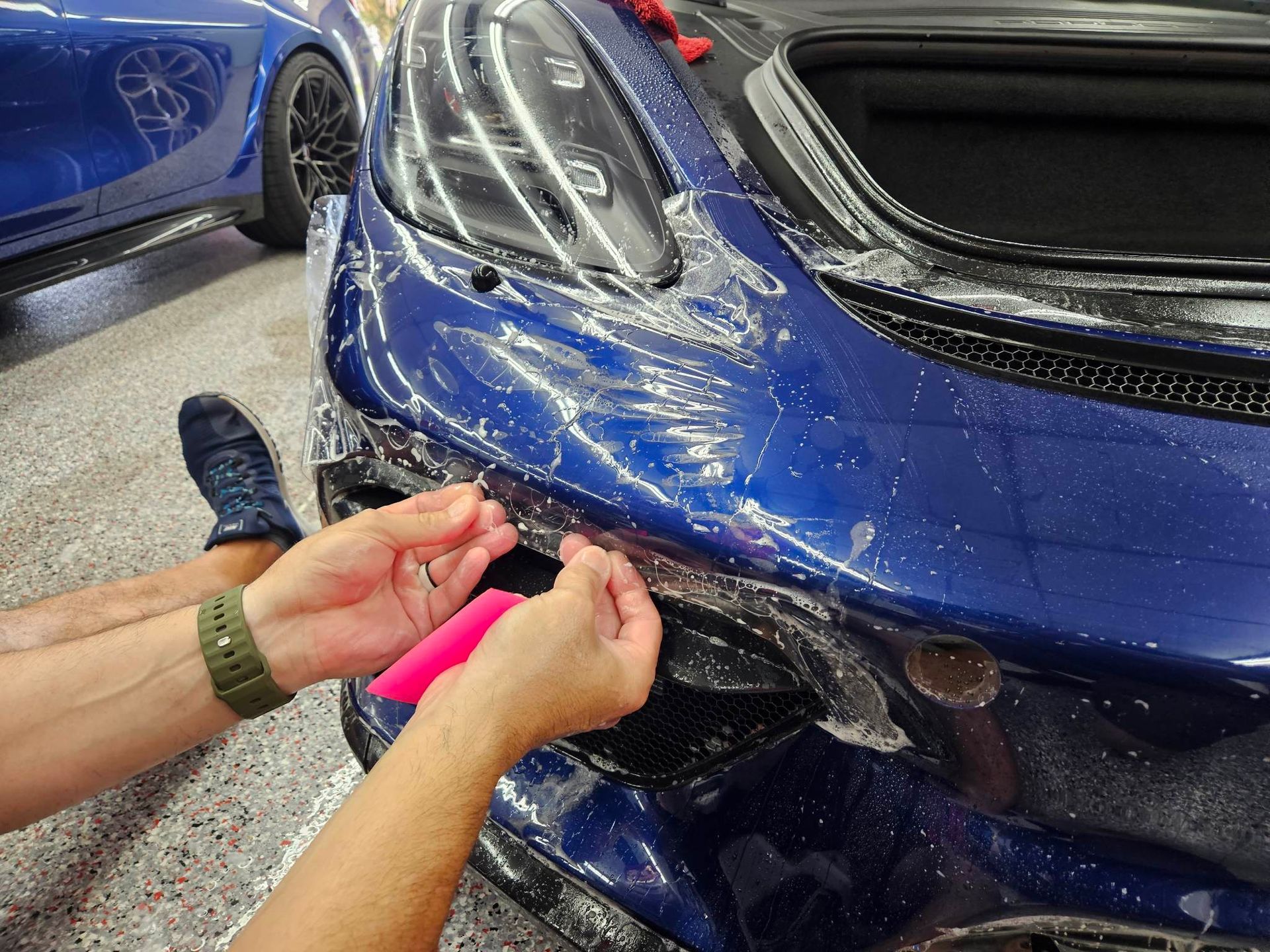 A person is applying a protective film to the front of a blue car.