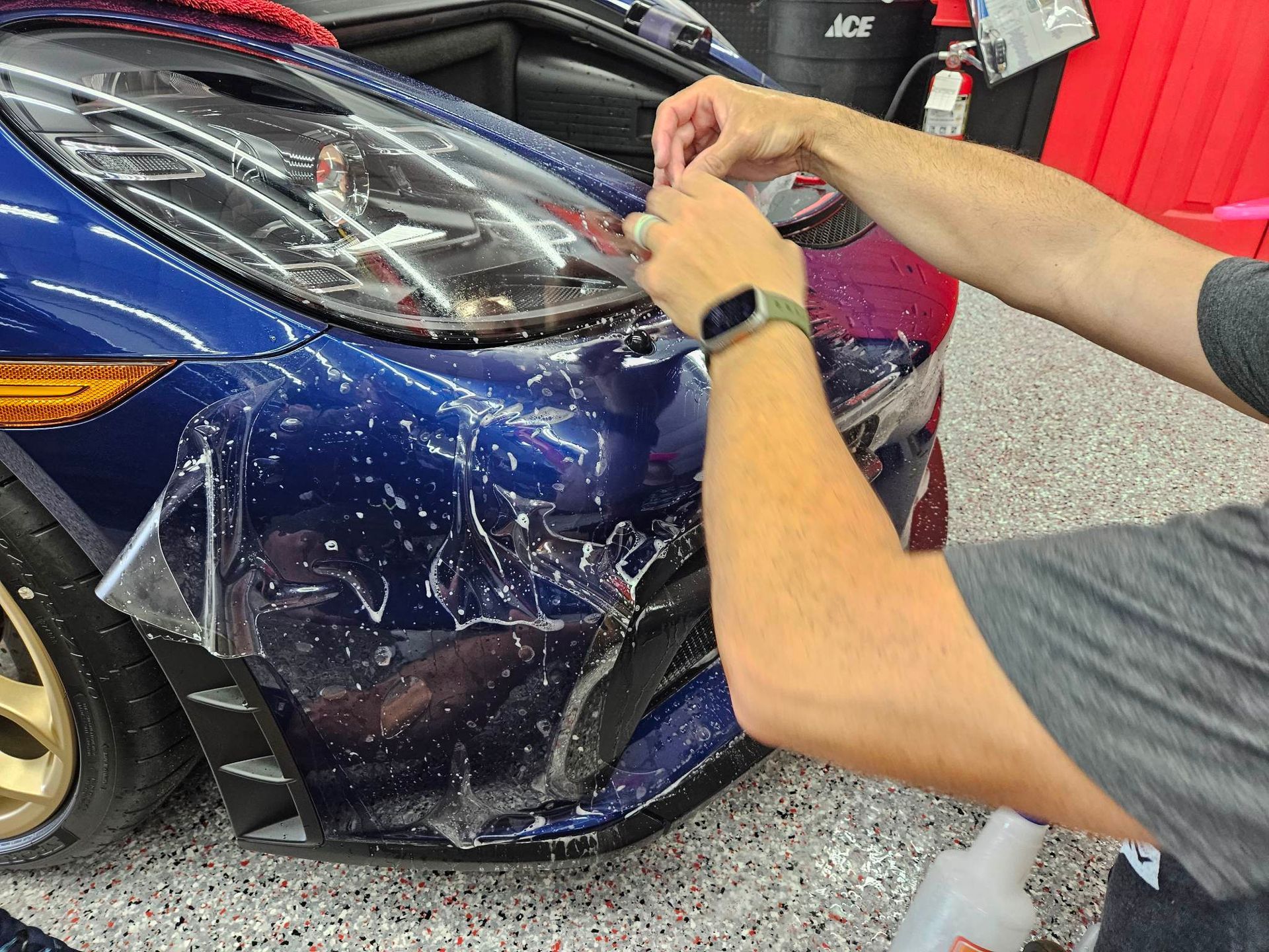 A man is applying protective film to the front of a blue car.