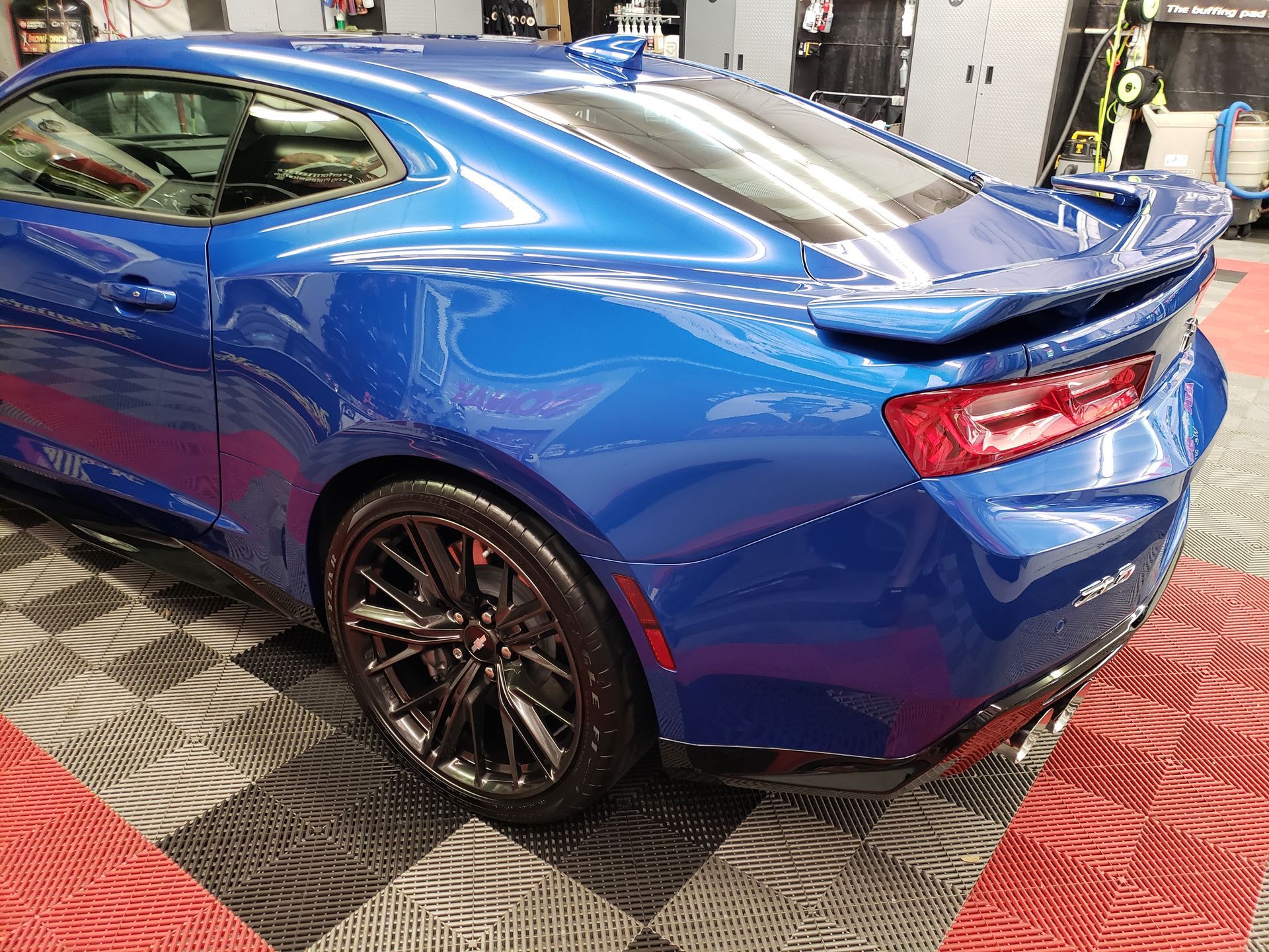 Blue sports coupe displayed indoors on a checkered floor, rear three-quarter view