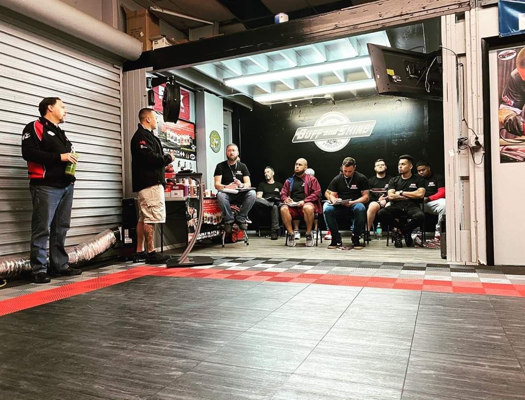 A group of people are sitting in a room in a garage.