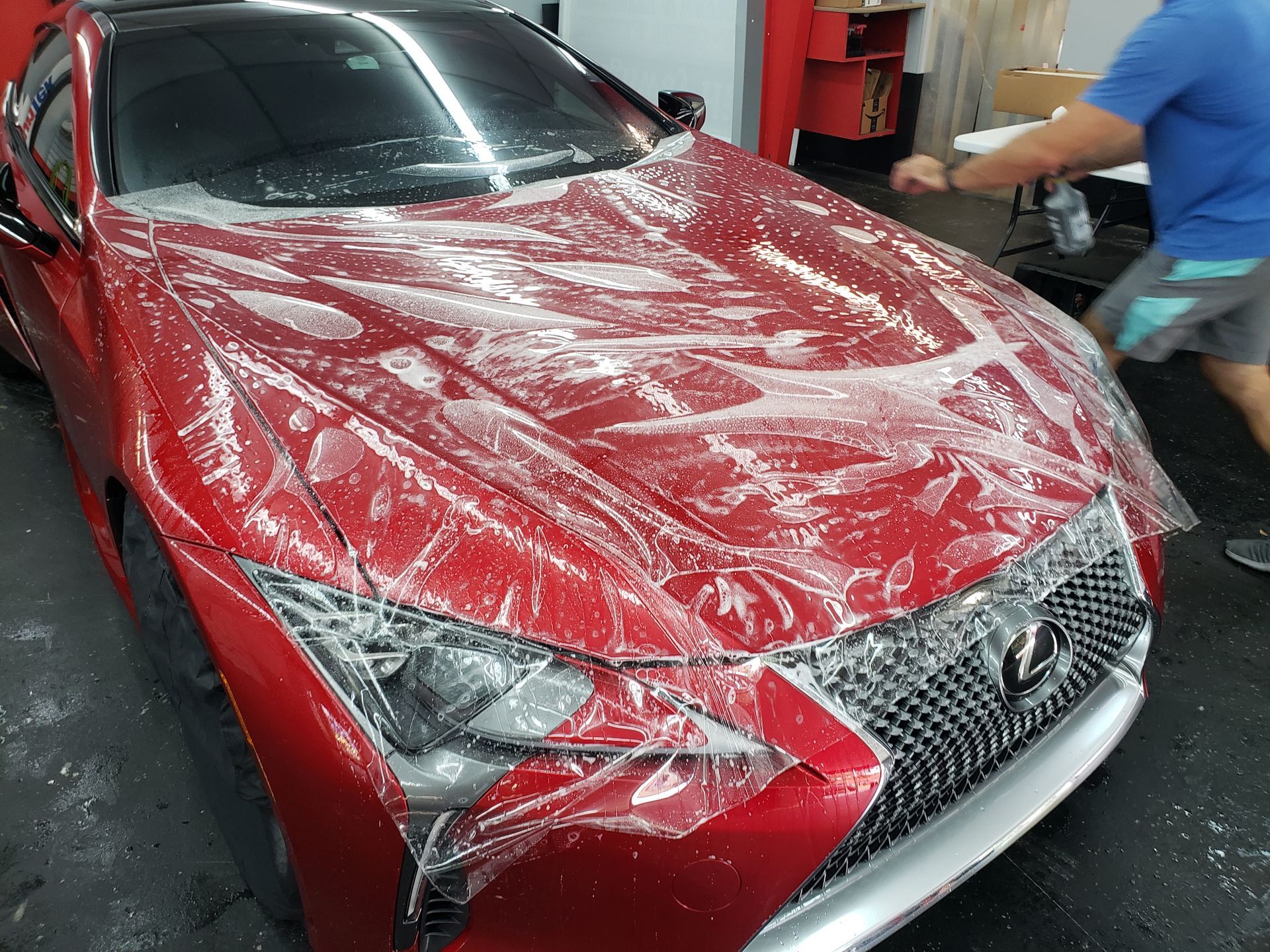 A red car is wrapped in plastic and a man is standing next to it.