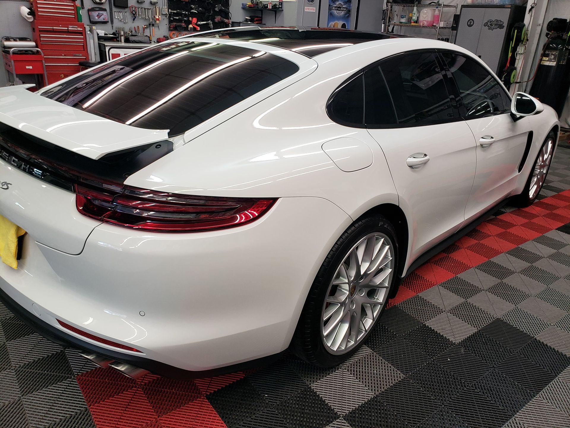 White Porsche Panamera sedan with tinted windows, parked indoors on a tiled floor.